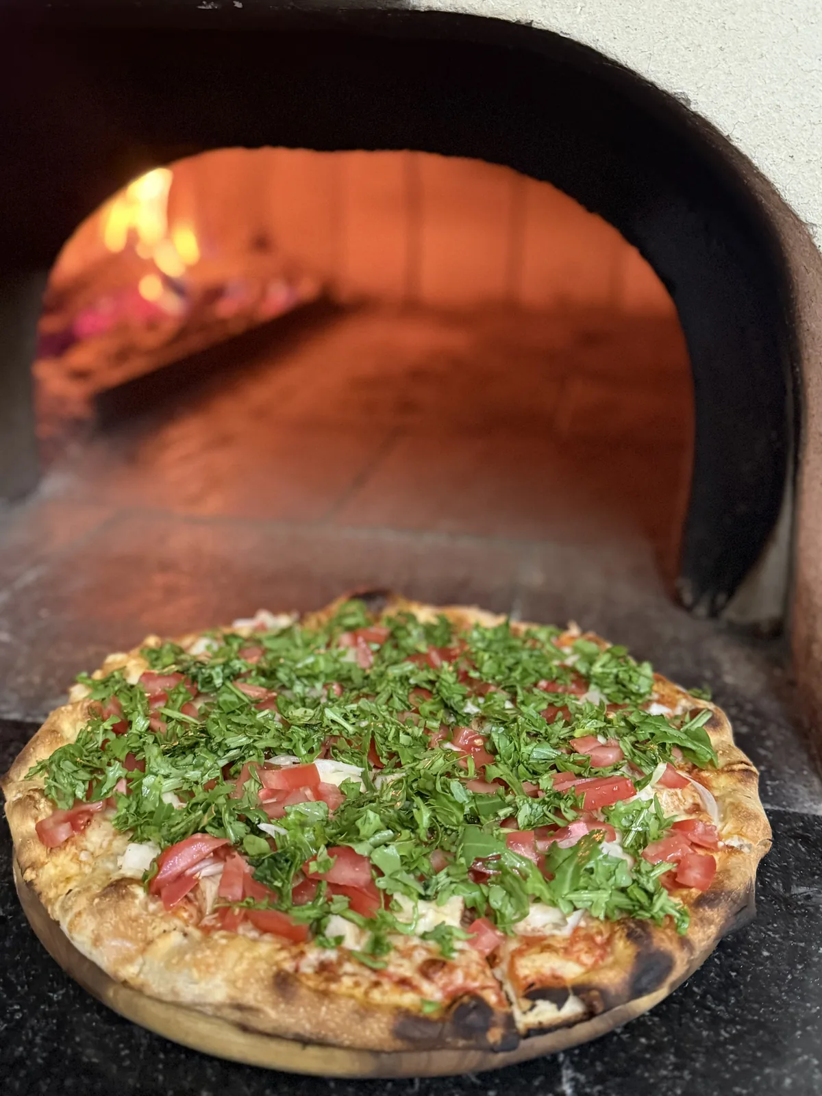 Frisch gebackene Pizza mit Tomaten und Kräutern vor dem Holzofen