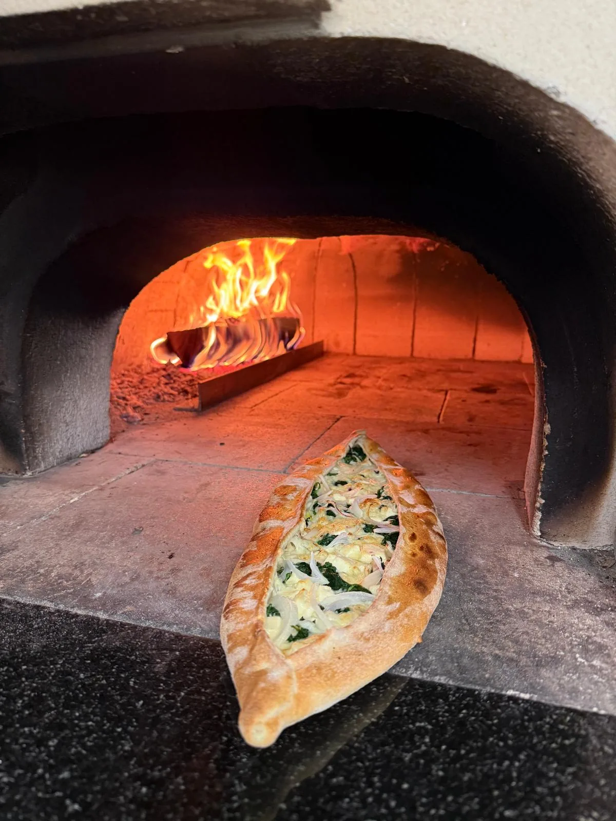 Spinat-Käse Pide im Holzofenbackofen mit Flammen im Hintergrund
