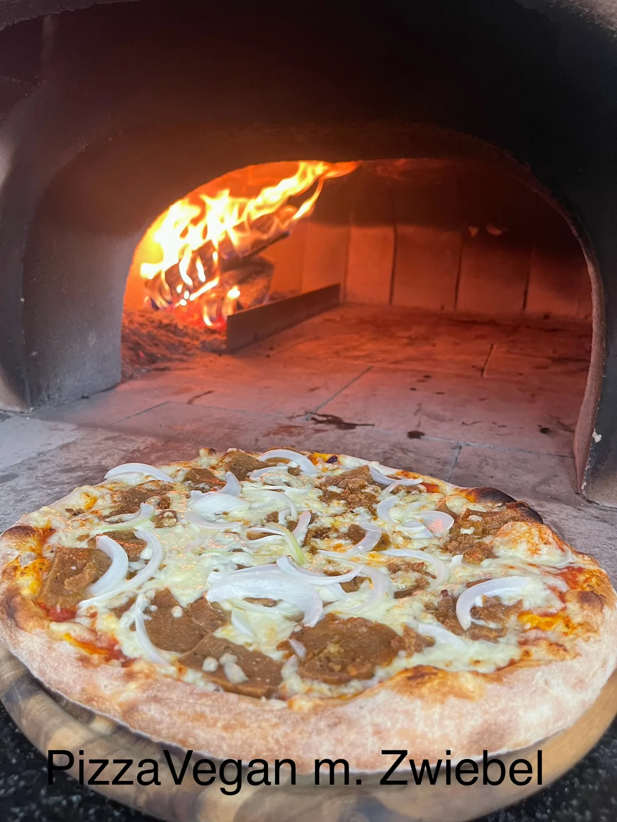 Vegane Pizza mit Zwiebeln und pflanzlichem Ersatz vor dem Holzofen